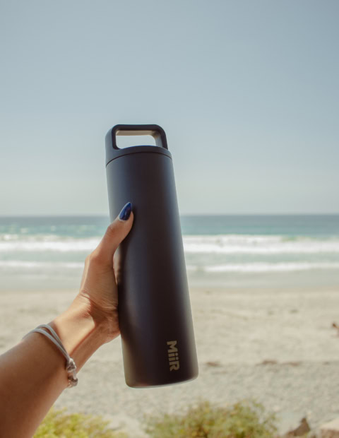 Schwarze Trinkflasche am Strand mit Logo-Design.